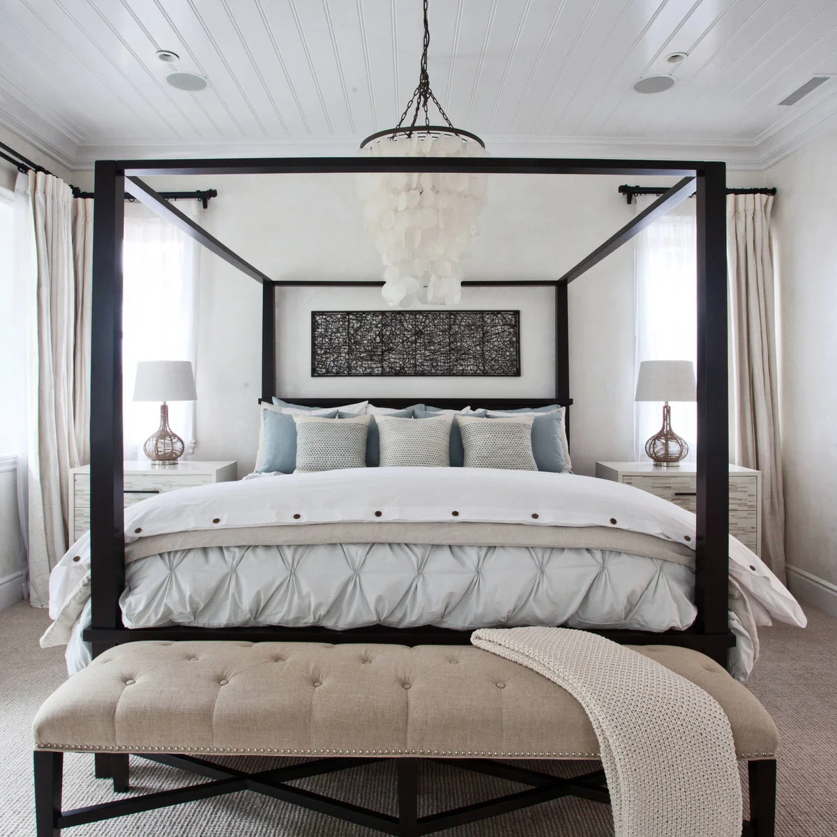 Beige tufted bench with black cross-braced legs beneath a dark canopy bed