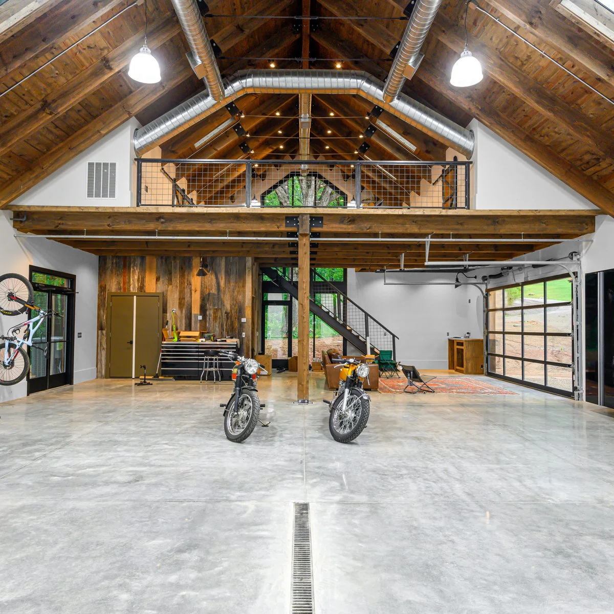 Large timber-roofed garage with motorcycles in the open center, a tool chest along the back wall and seating to one side.