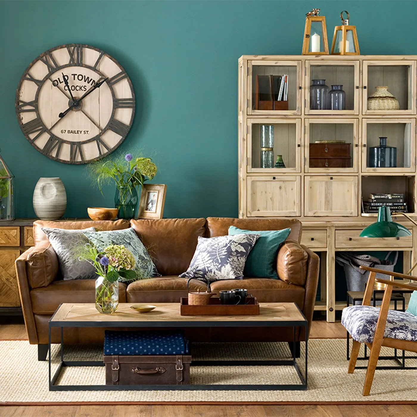 Brown couch with pale botanical, dark floral and green pillows beneath a turquoise wall.