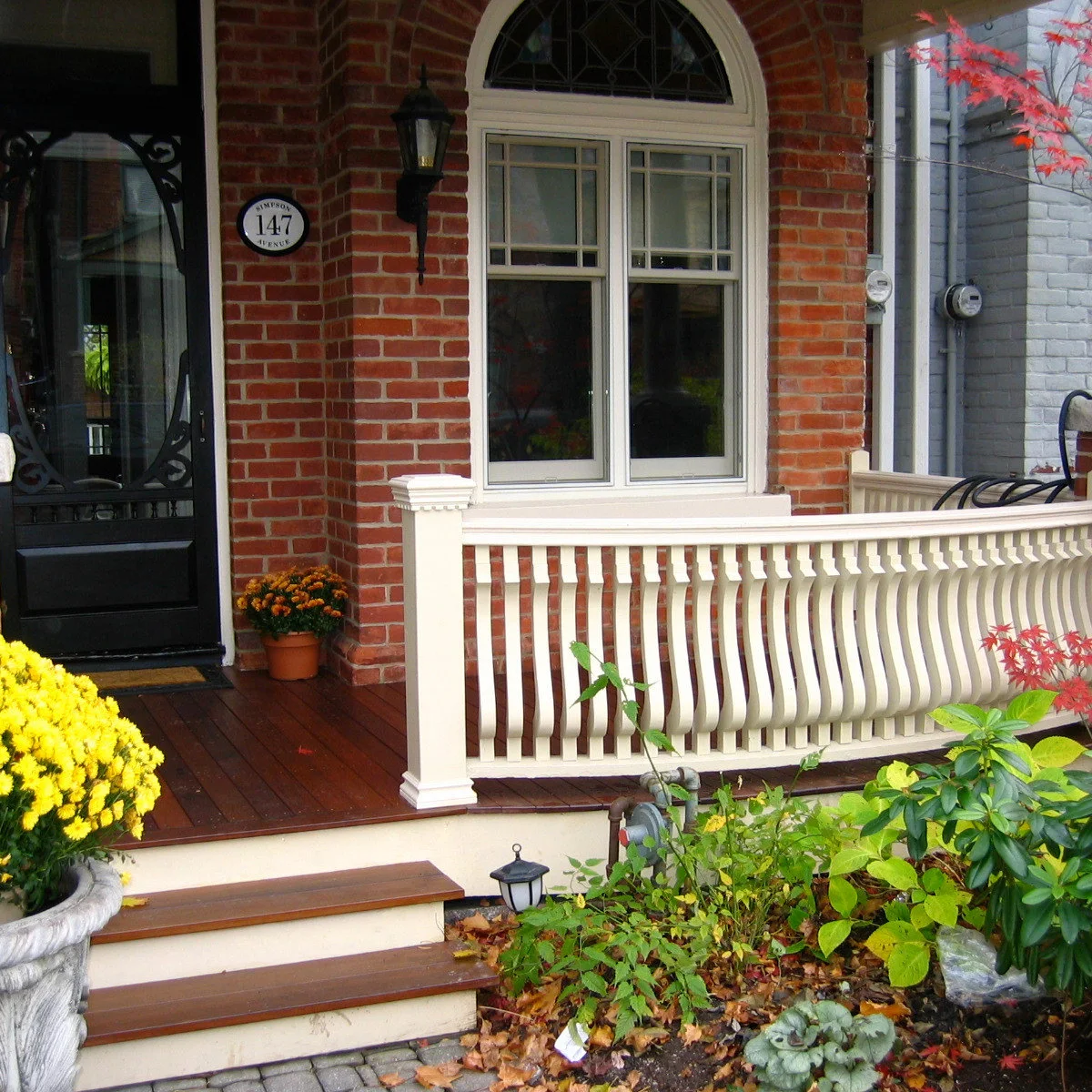 Compact brick front porch with a pale railing, dark door and planted beds beside the steps