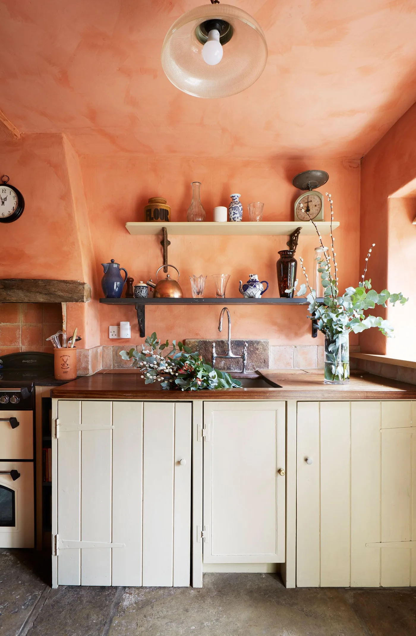 Orange kitchen walls and ceiling above pale paneled cabinets, open shelves and a wooden counter.