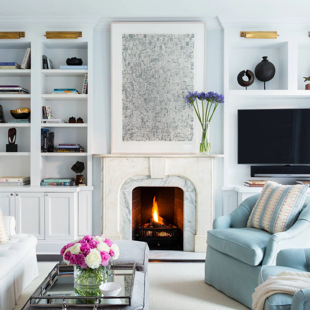 A pale fireplace with a large artwork above it and a television on the neighboring white built-in cabinet.