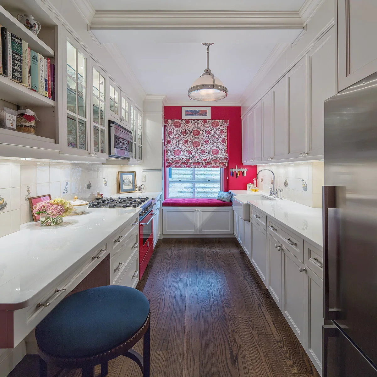 White galley kitchen with red end wall, patterned shade and window seat