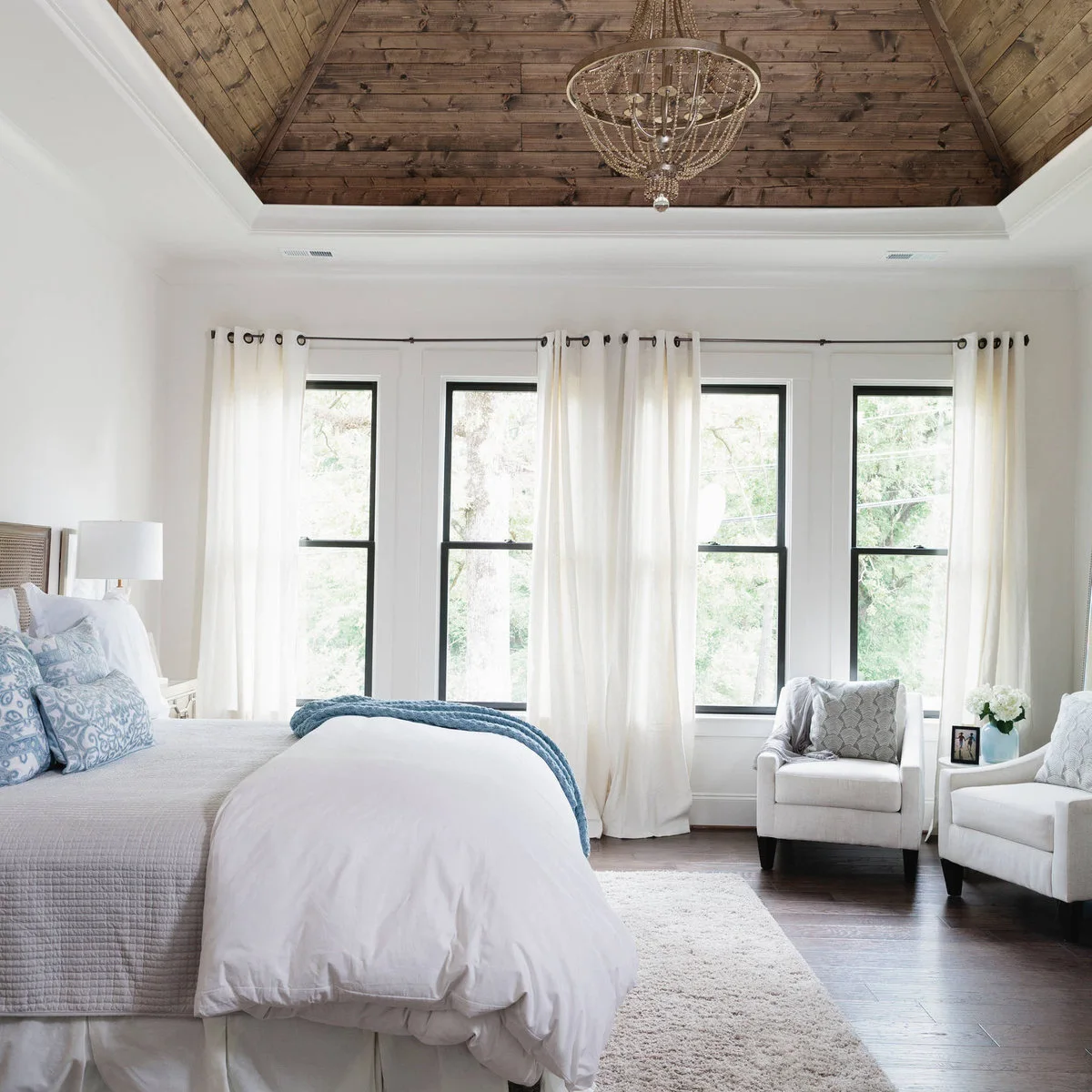 Wood boards inside a bedroom tray ceiling above blue bedding and a beaded pendant