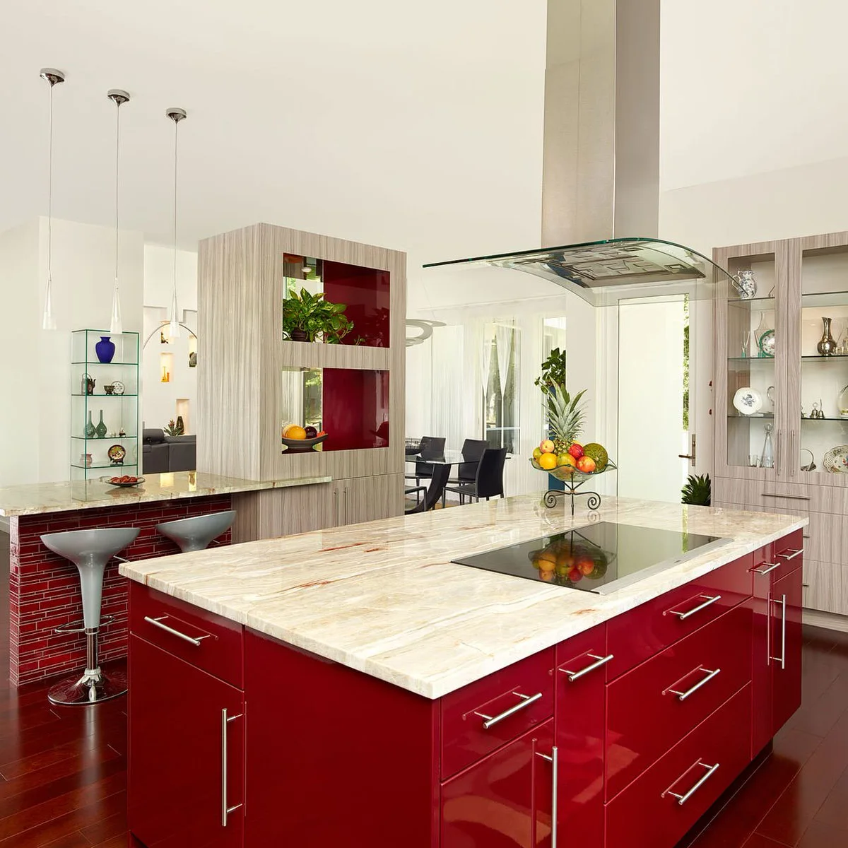A glossy red island with a pale patterned counter sits beside pale gray-brown display cabinetry and a red-tiled breakfast bar.