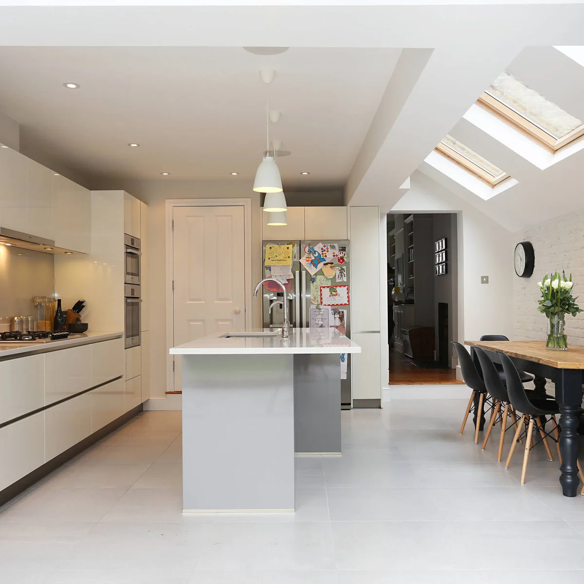 White terrace-house kitchen with a central sink island and a wood-colored dining table under rooflights