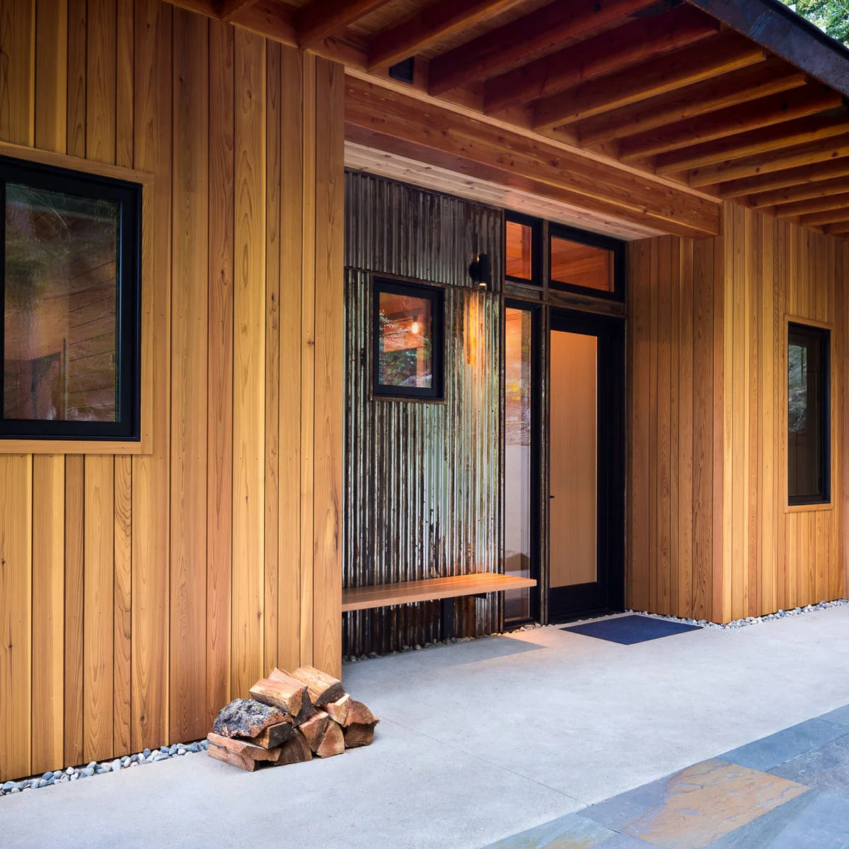 Wood-sided covered entrance with a narrow wall bench beside a dark front door