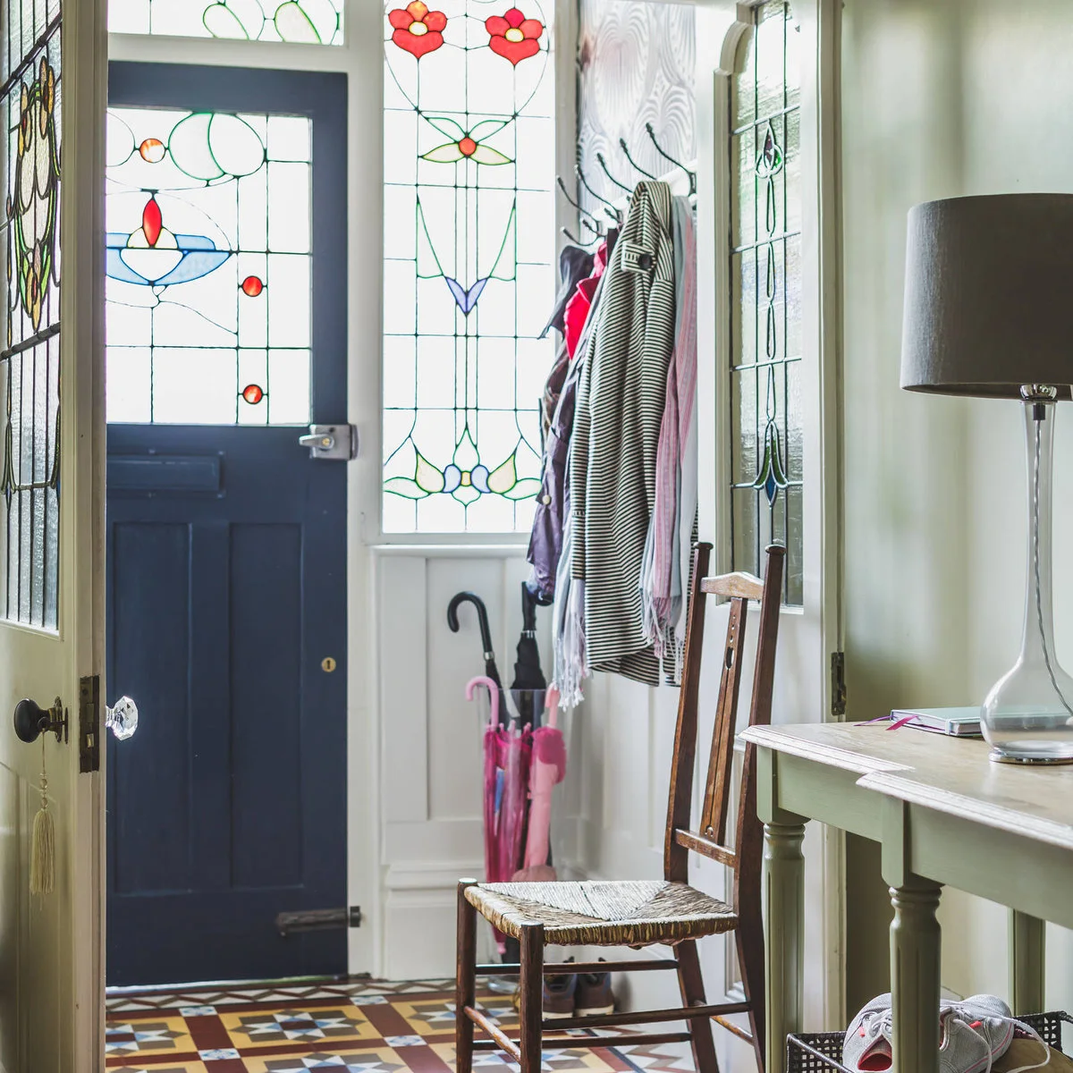 Compact entrance with stained-glass door panels, a dark blue door, pale green walls and a wooden chair.