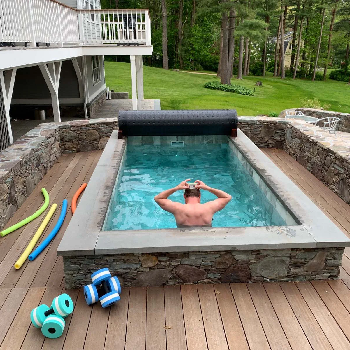 A raised plunge pool with a stone-faced exterior sits in a wood deck, with a rolled cover at the far end and garden walls beyond.