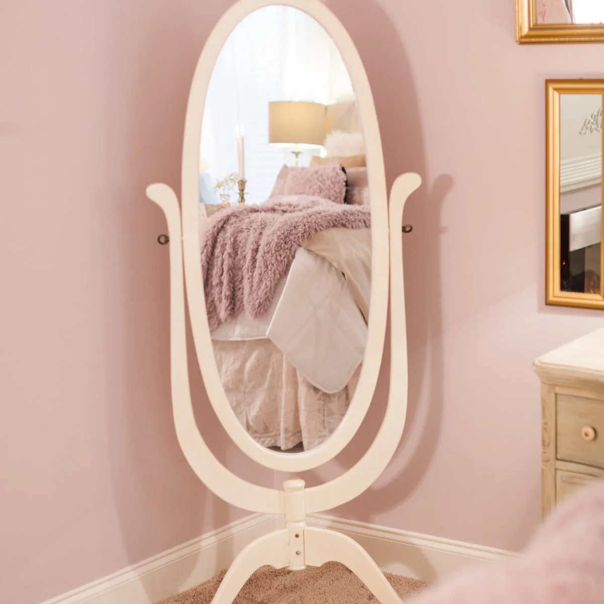 Oval pale standing mirror against pink walls reflecting a bed with a textured throw