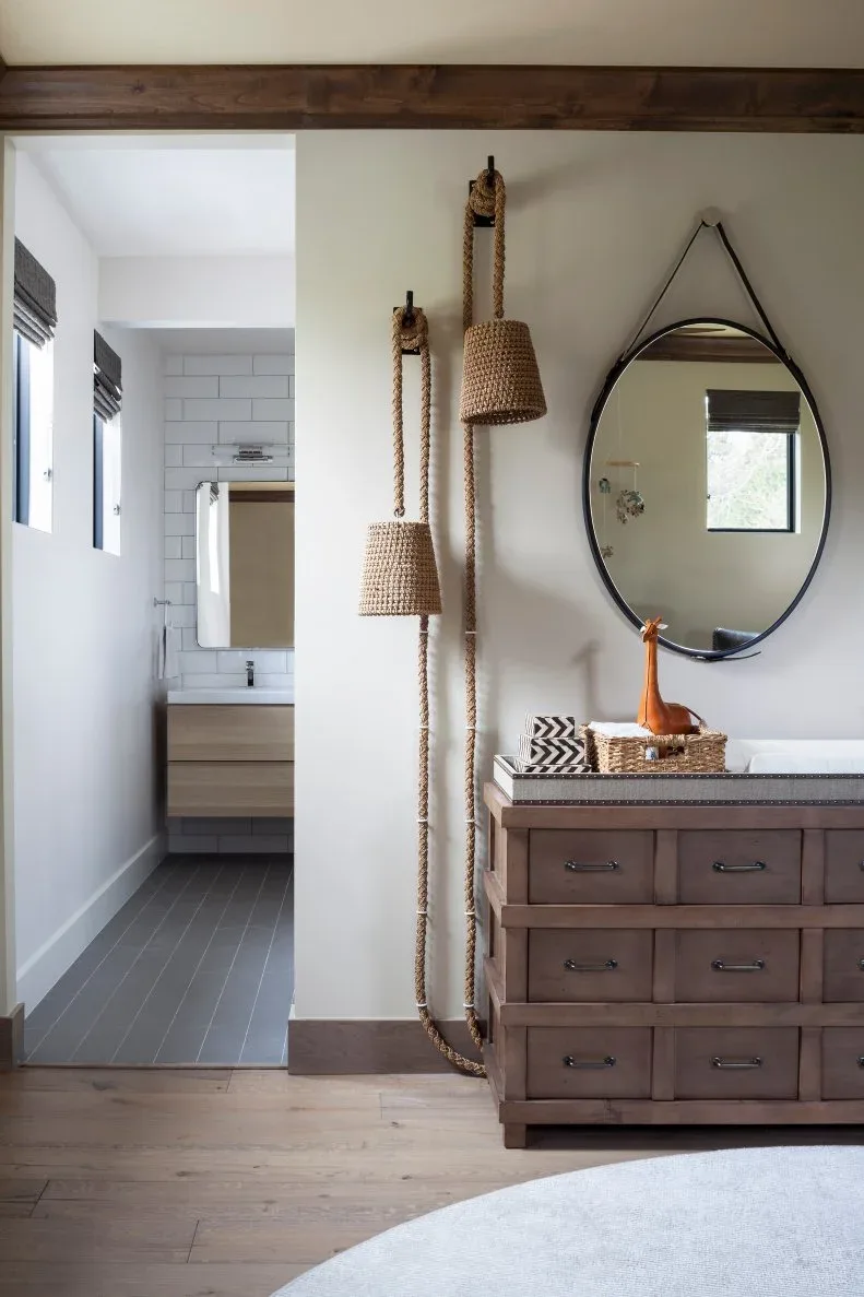 Warm wooden drawers beneath round mirror beside woven-looking hanging shades and rope detail.