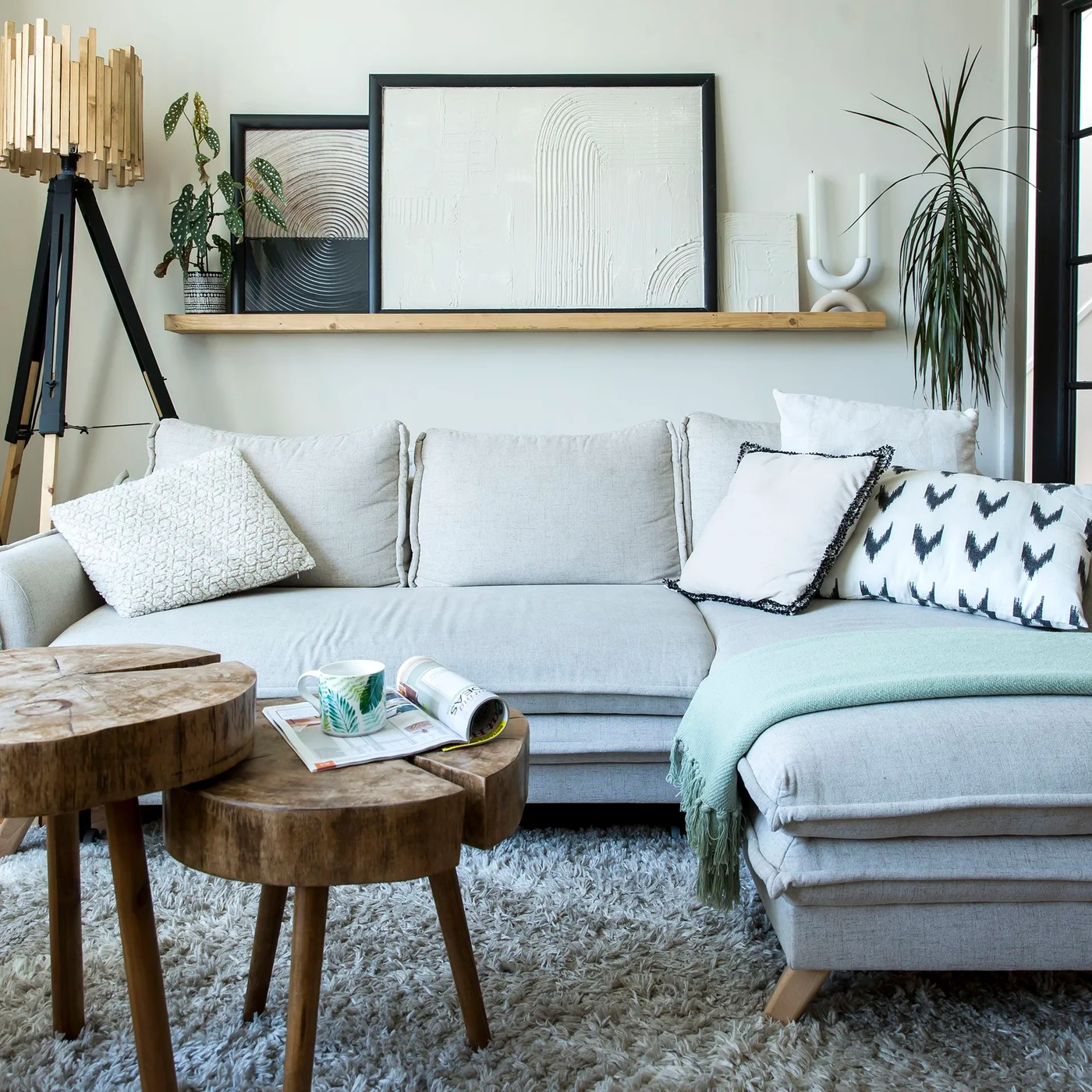 A pale sectional with patterned cushions sits beneath textured framed artwork beside two round timber tables.