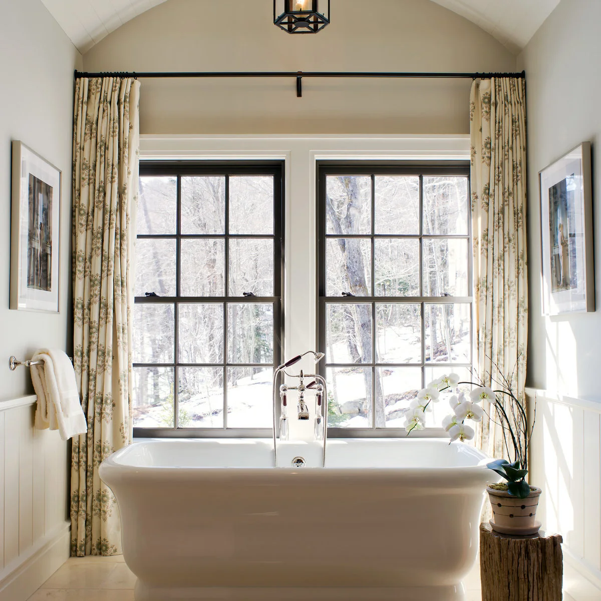 Long pale floral curtains hang from a black rod above two black-framed windows behind a white bath.
