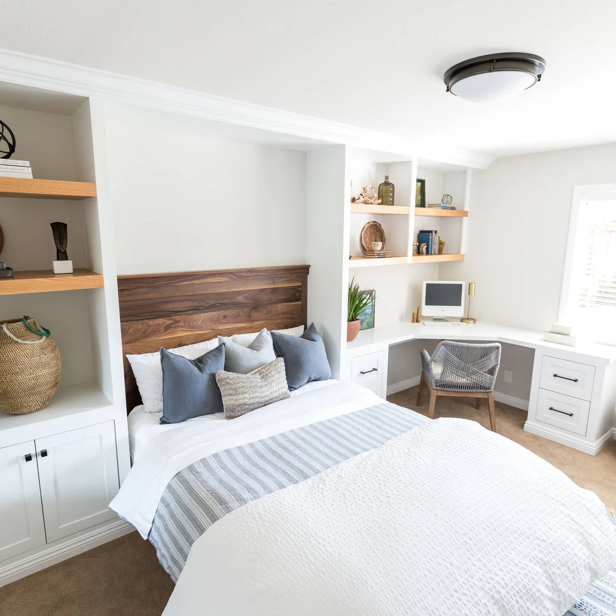 Small white bedroom with a wood headboard, fitted shelves and a corner desk beside the window