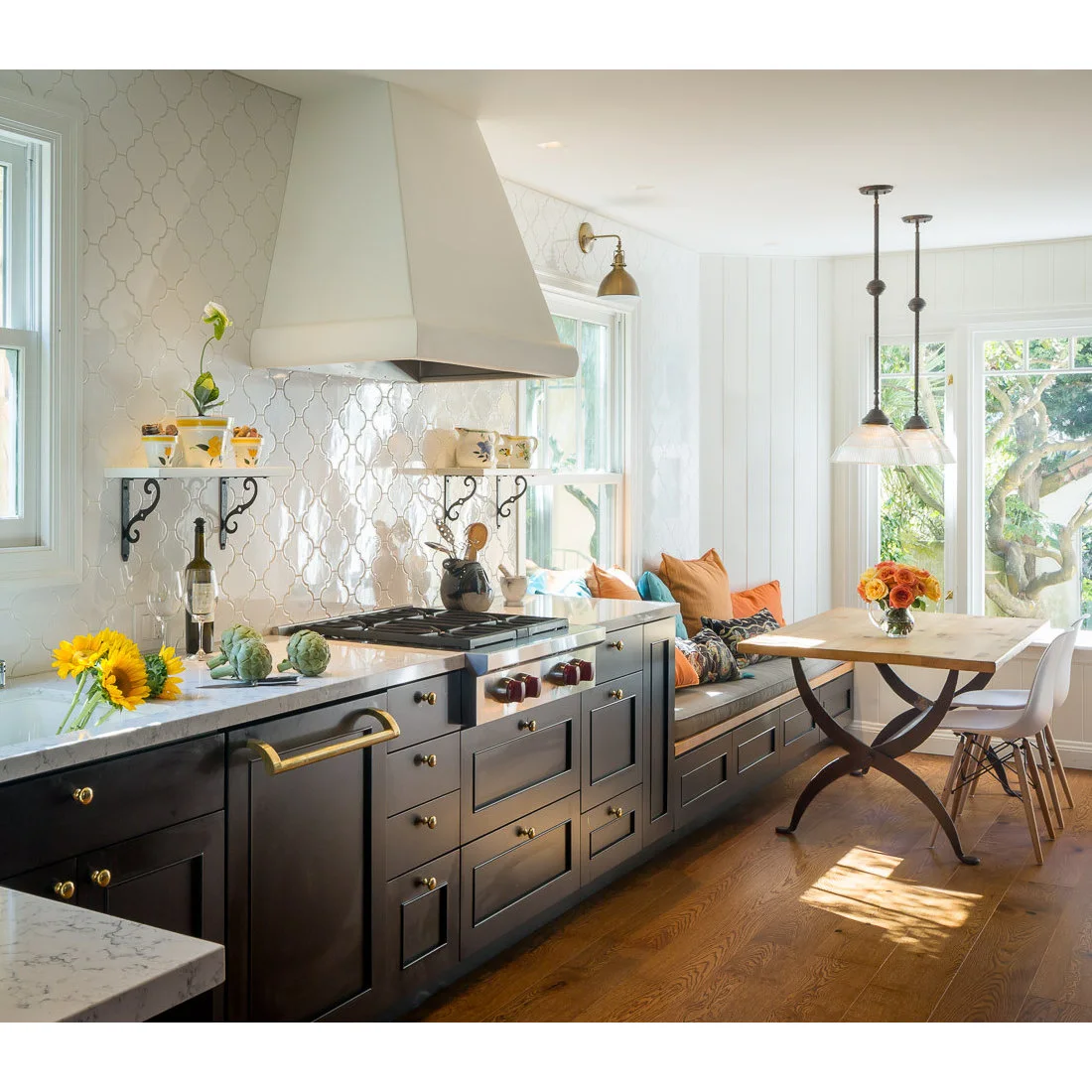 Dark cabinets and pale curved-pattern tiles lead toward a window-side bench and a small kitchen table.