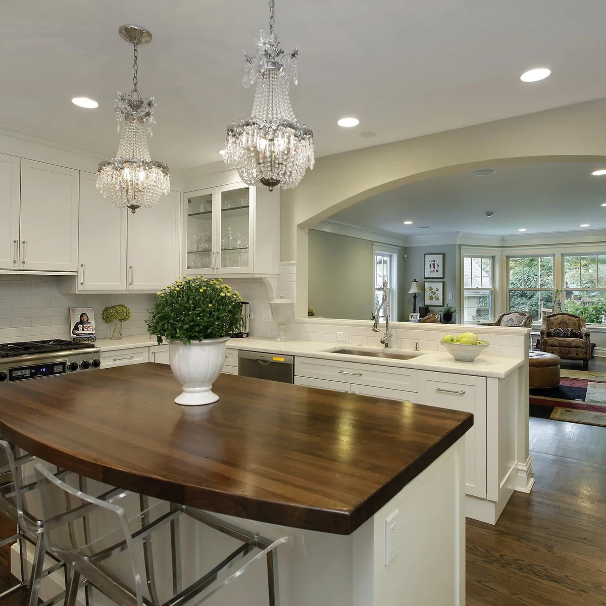 An arched opening and low tiled wall connect a cream kitchen with the sitting room beyond.