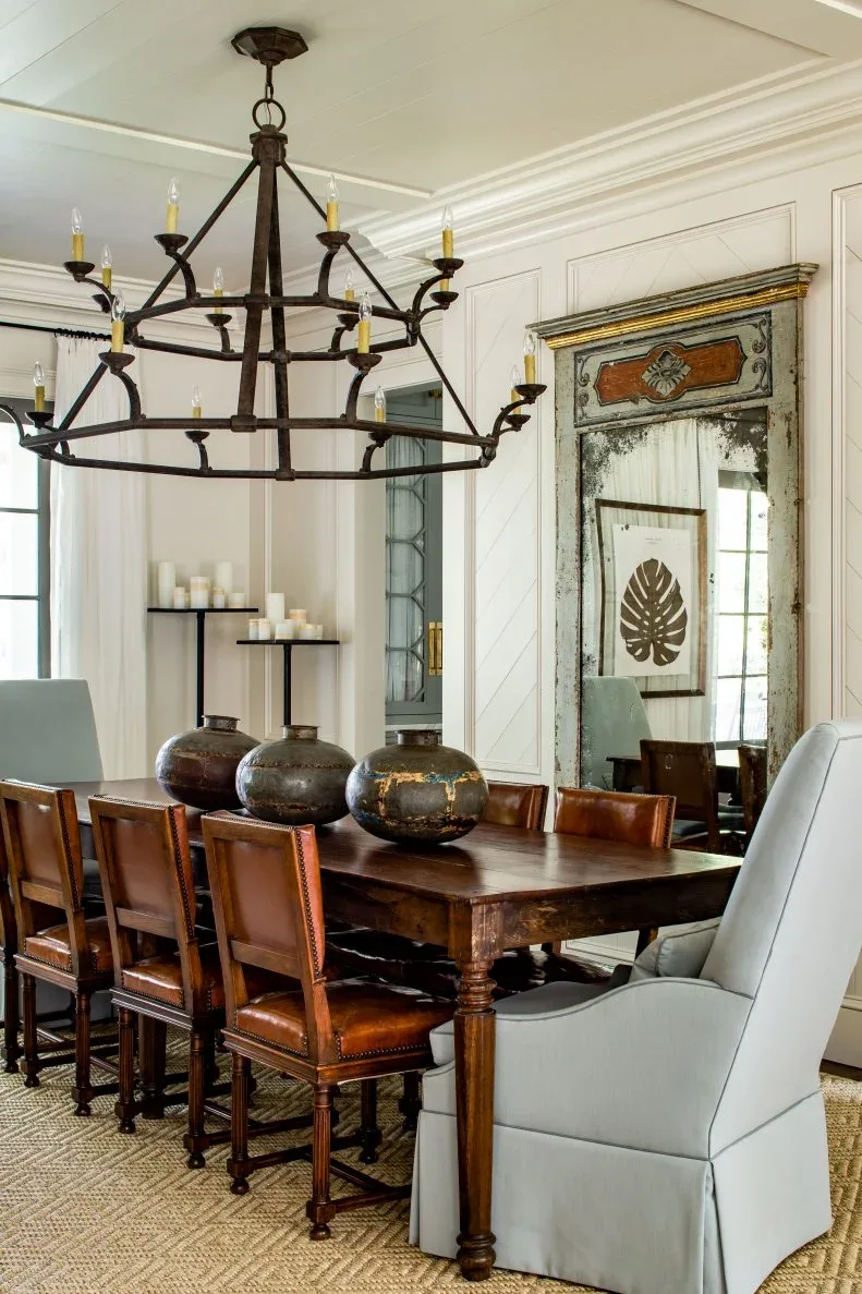 Three rounded dark decorative pots on a wood dining table with brown chairs and pale upholstered end seats
