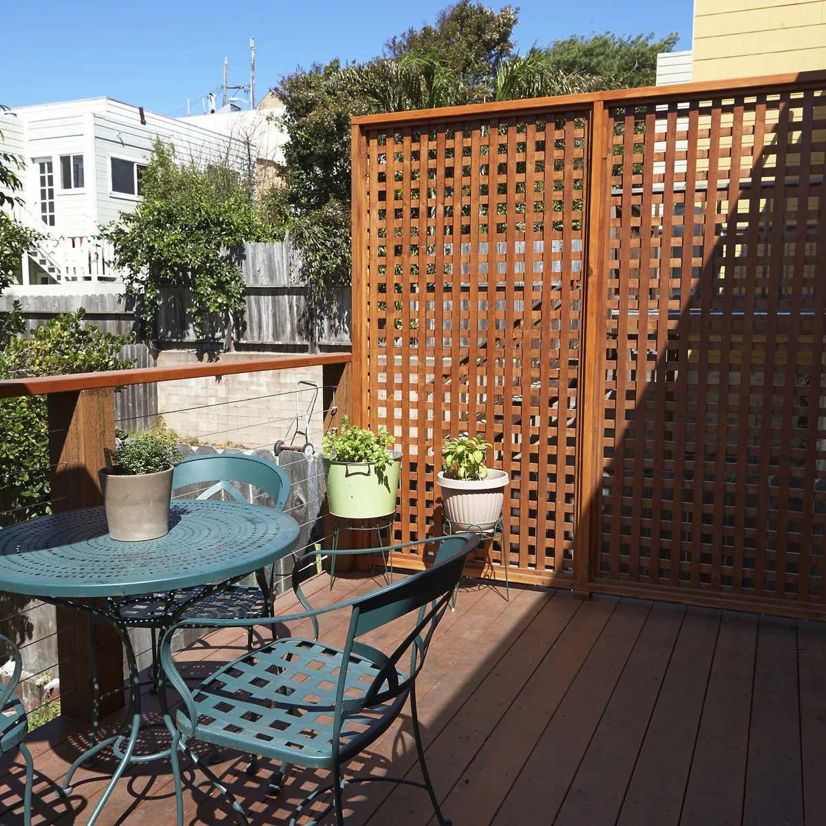 A tall warm-wood lattice panel stands beside a blue-green bistro table on an elevated deck