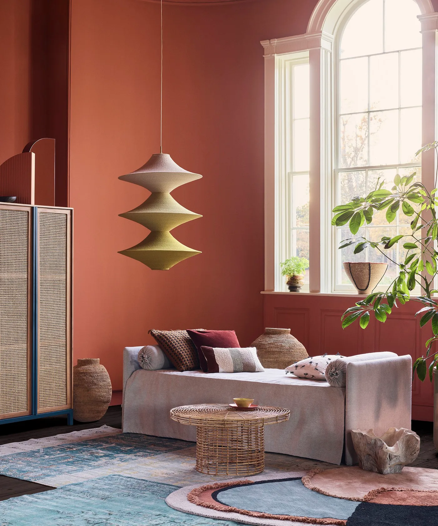 Clay-colored walls around a pale daybed with woven baskets, a round woven table and leafy plants