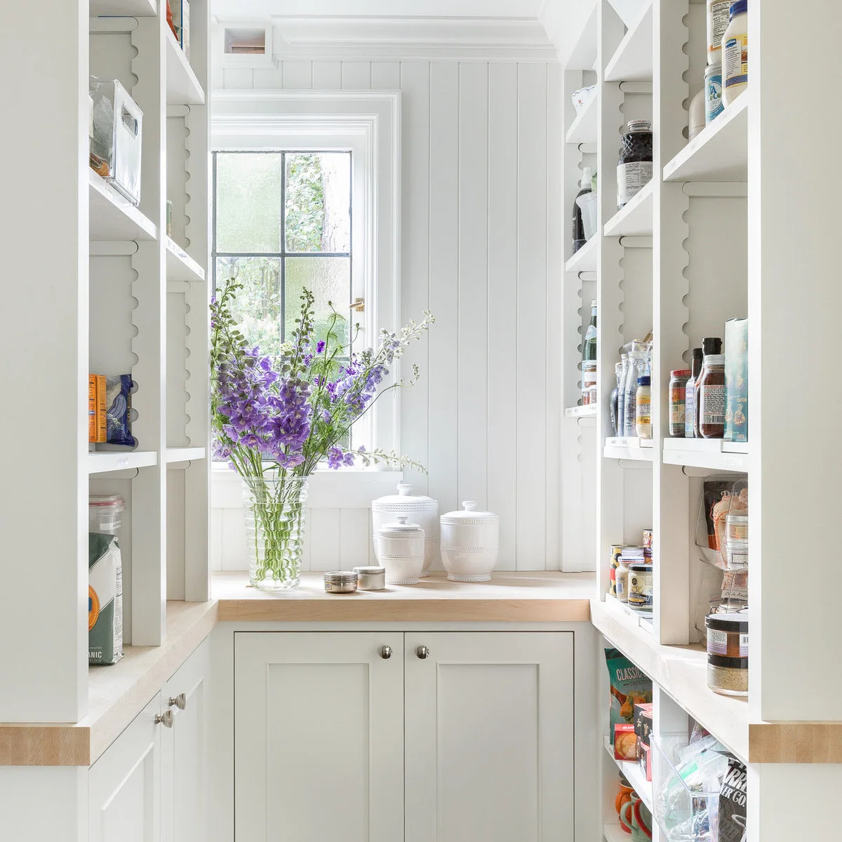 Narrow white pantry with shallow side shelves and a window above an end counter