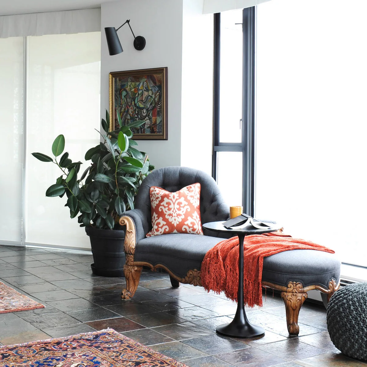 Gray chaise beside a small black pedestal table, black wall light and potted plant