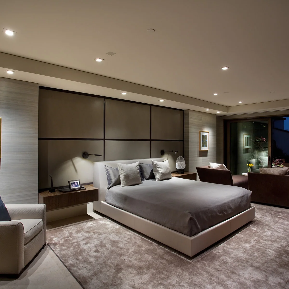 Modern bedroom with grey bedding, a broad framed headboard wall and wood bedside cabinets