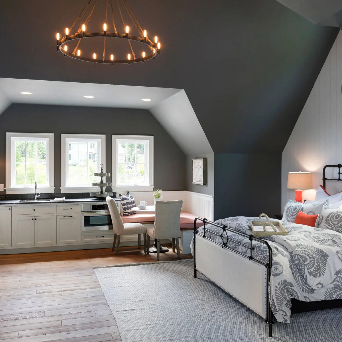 Compact kitchenette beside a window and dining bench in a studio with a bed beyond