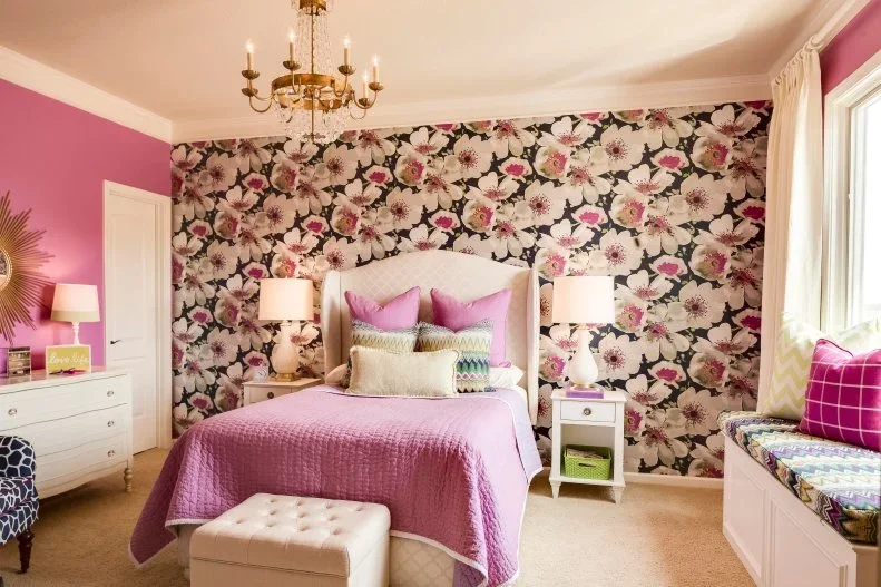 Pink flowers on dark wallpaper rise behind a pale bed between pink painted walls and a window seat.
