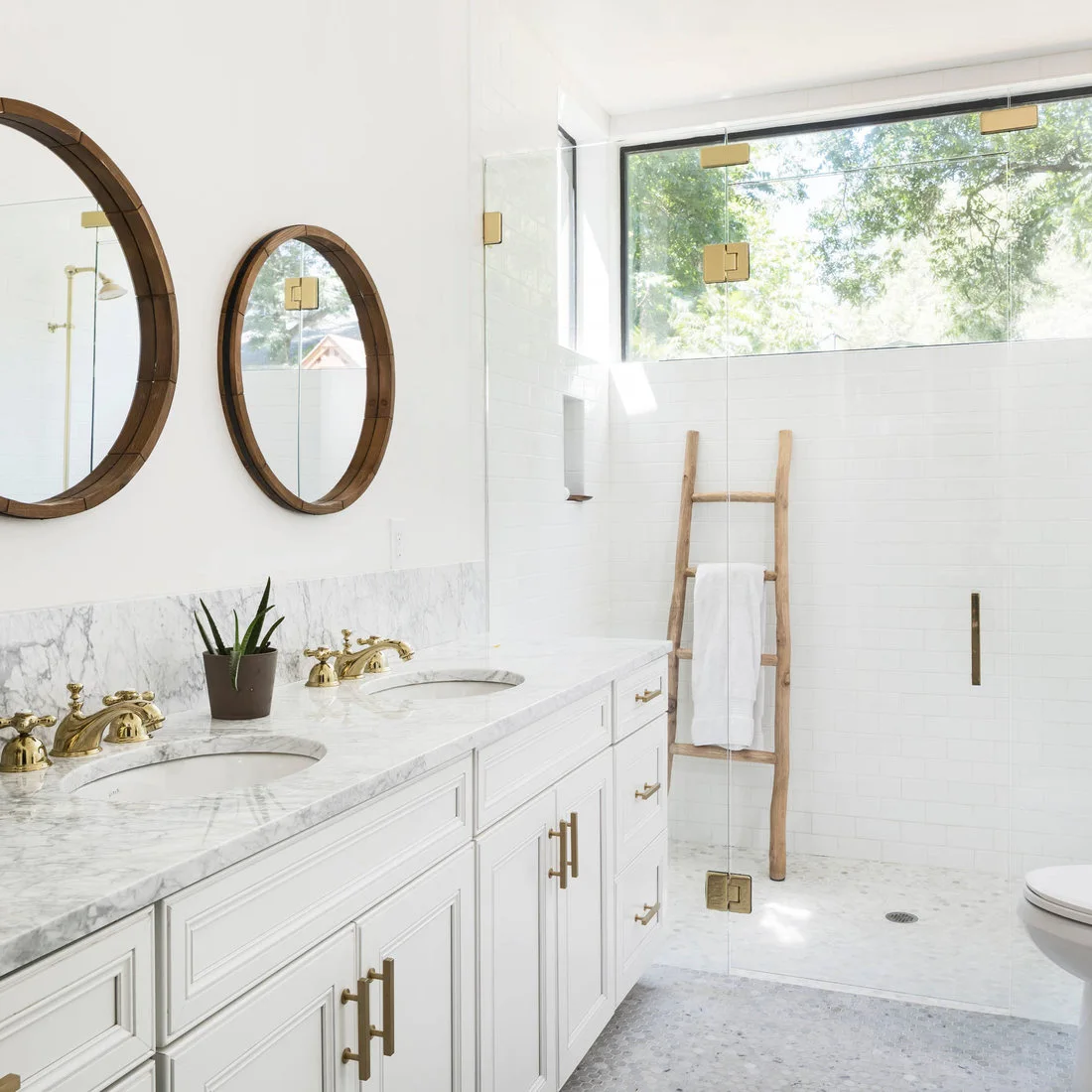Small pale hexagonal mosaics cover a bathroom floor below white cabinets and rectangular shower wall tiles.