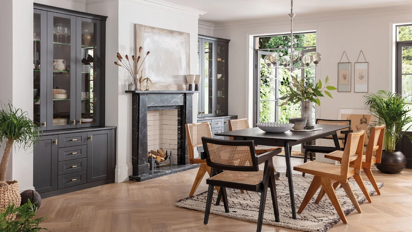 A dark veined marble fireplace stands between dark glass-front cupboards in a pale dining room.