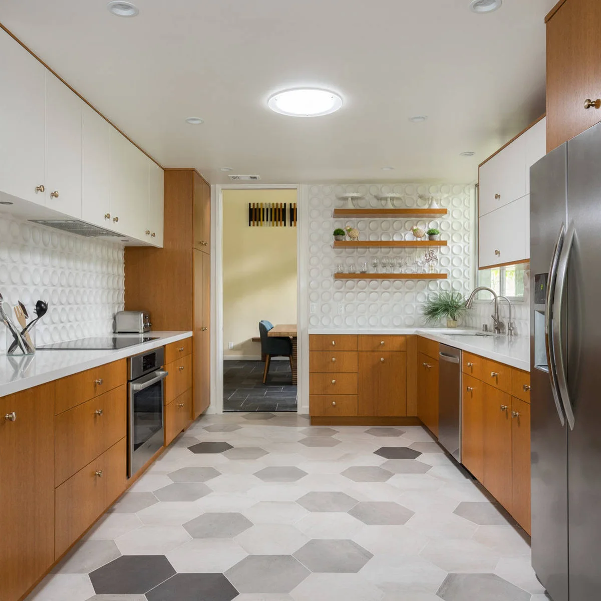 Honey-toned lower cabinets, white uppers and rounded white textured backsplash tiles in a compact kitchen.