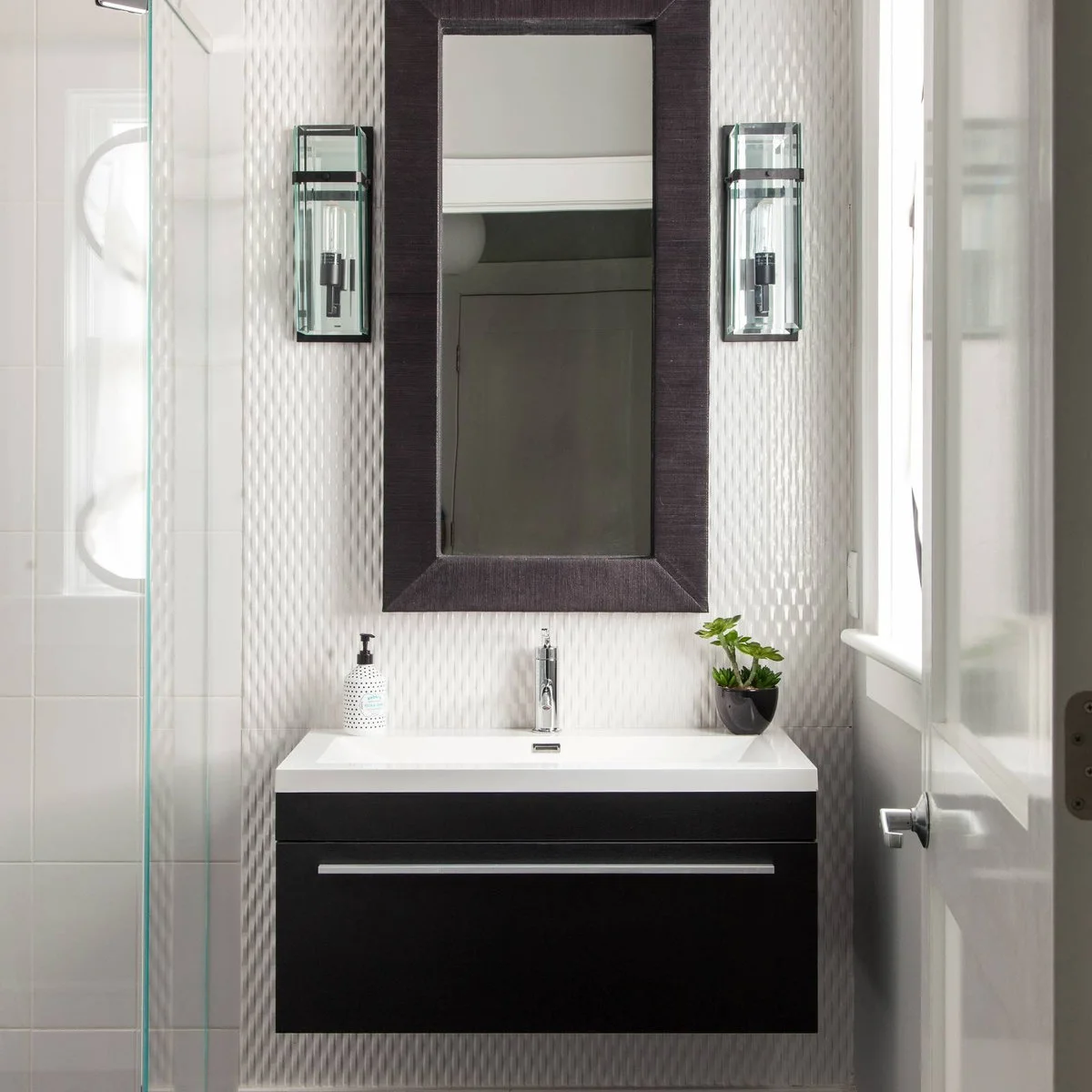 Tall dark-framed mirror between glass wall lights above a black floating vanity
