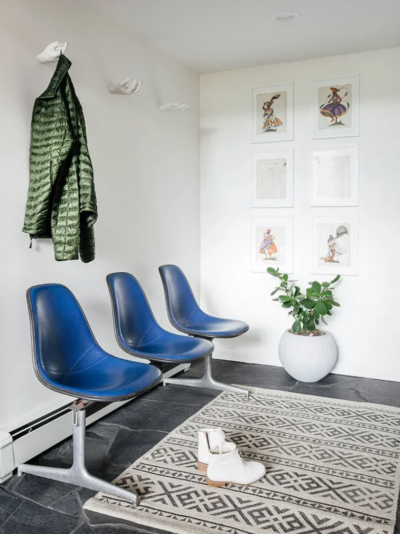 Mudroom corner with three blue molded seats on shared base, small framed pictures, sculptural wall hooks and geometric rug.
