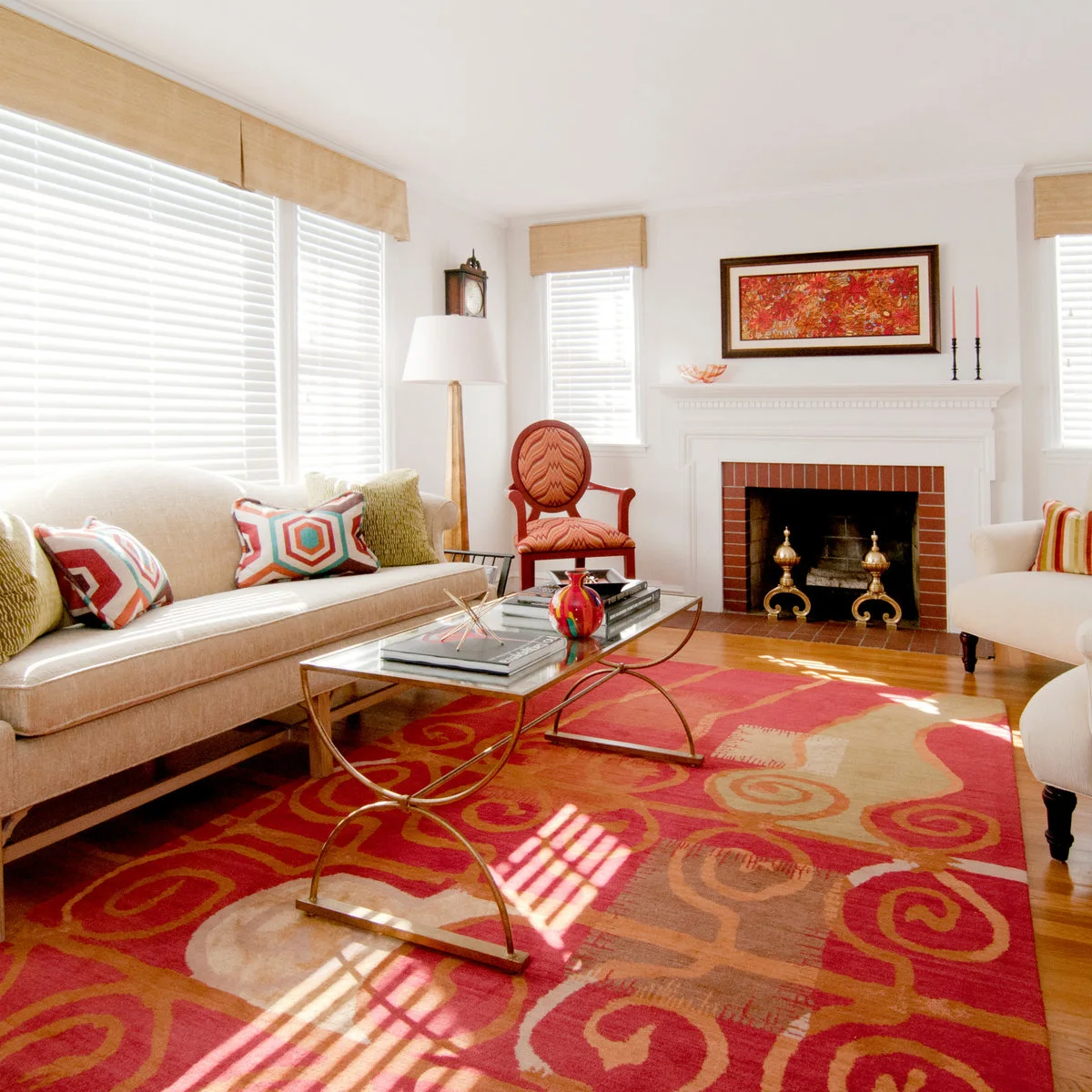 A red brick inset within a pale mantel is surrounded by pale sofas, a red patterned rug and a red-framed accent chair.