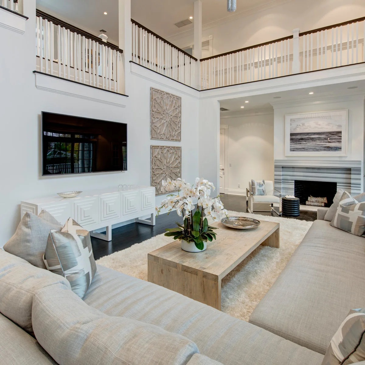 An L-shaped pale sofa faces a television on a long wall, with a fireplace and single chair at the end of the room.