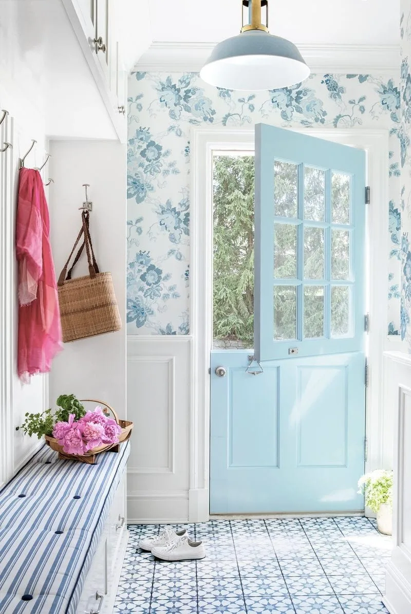 Blue floral wallpaper around a pale blue divided door with striped bench cushions and patterned floor tiles.