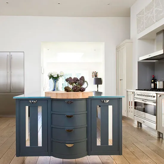 A blue painted island with metal handles stands within pale cabinetry