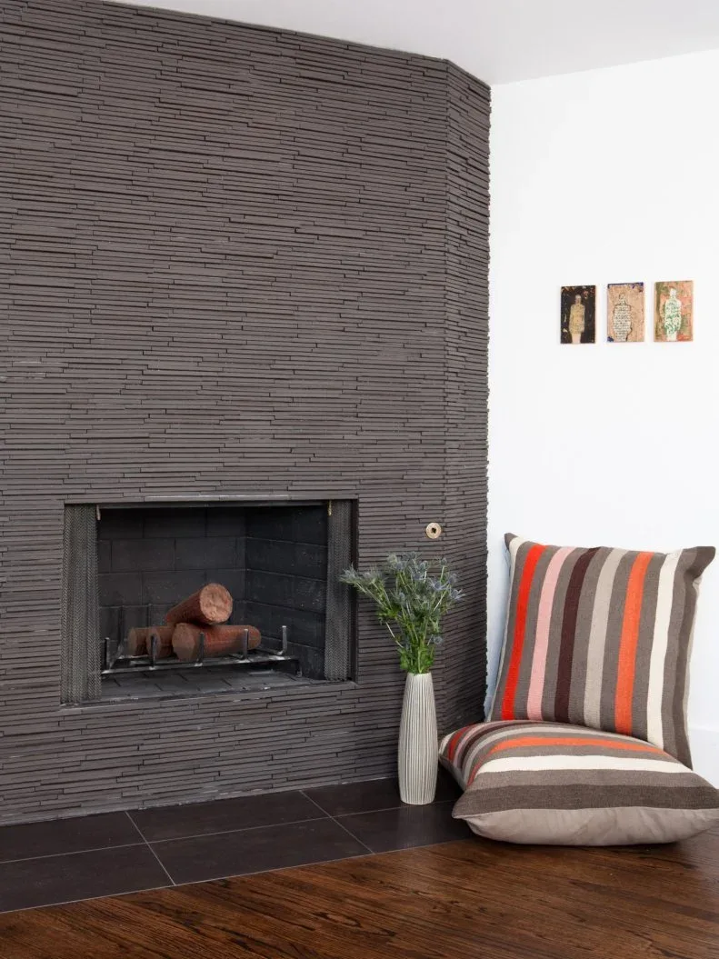 Dark gray horizontally textured fireplace wall with black opening, hearth and striped floor cushion