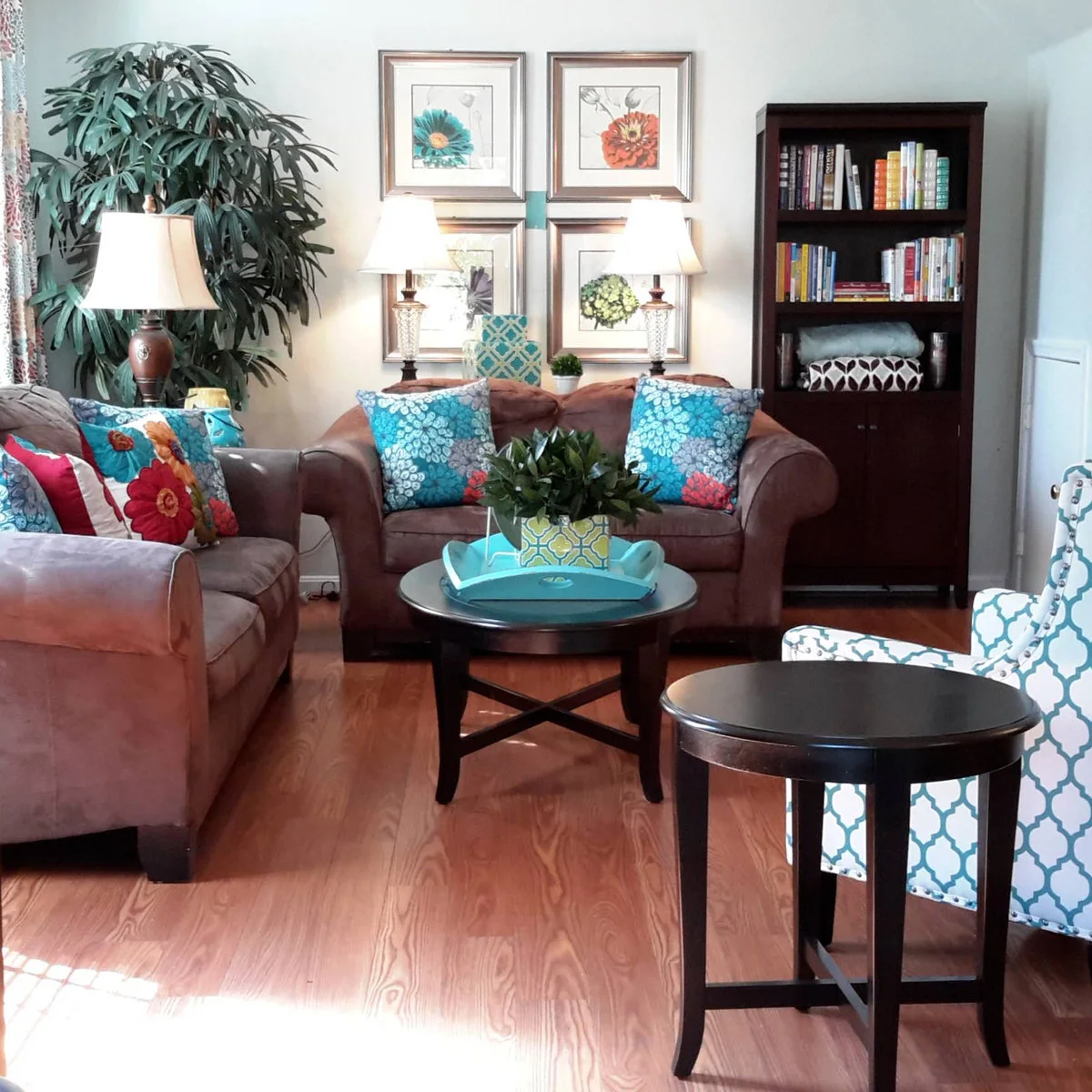 Brown rolled-arm sofas with teal patterned cushions, a teal and white chair and black round tables.