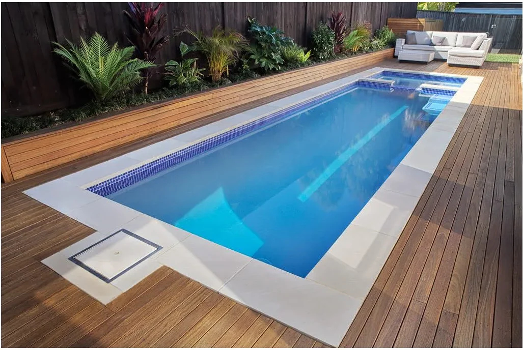 A narrow rectangular pool with blue waterline tiles sits beside wood decking, with a small spillover spa at the far end.