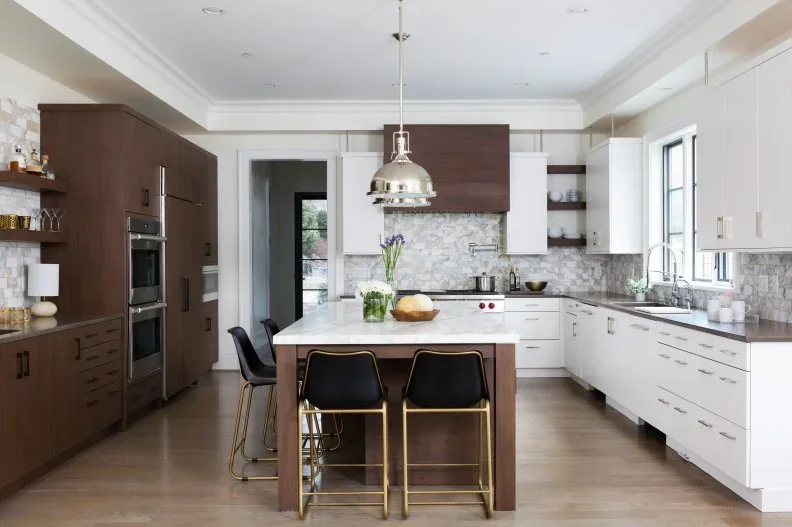 Brown wood tall cabinets face white cupboards across an island that combines wood panels with a pale top in a bright kitchen.
