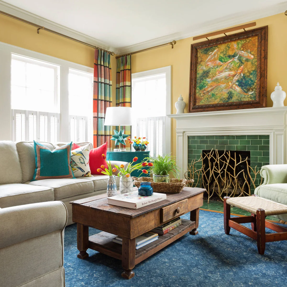 Yellow-walled living room with pale seating, teal cushions, red accents, patterned curtains and green fireplace tile