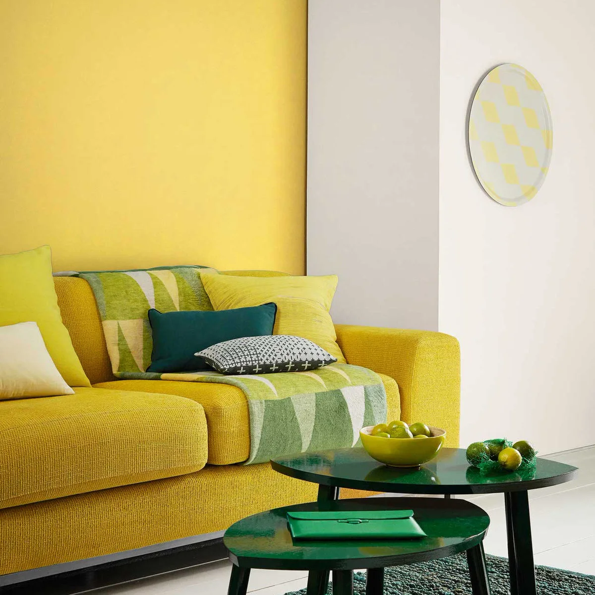Bright yellow sofa against a yellow panel and white wall with green cushions and dark nesting tables