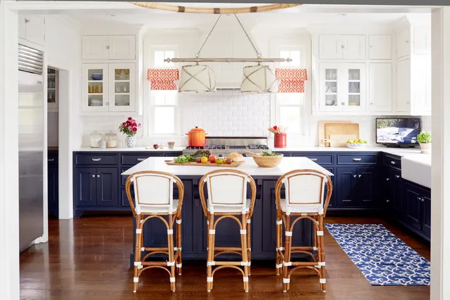 Deep blue cabinets frame a pale island beneath warm decorative lighting and cane-backed stools.