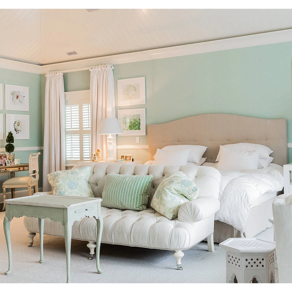 Pale mint bedroom with cream curtains and bedding, a cream sofa at the bed foot and a mint side table