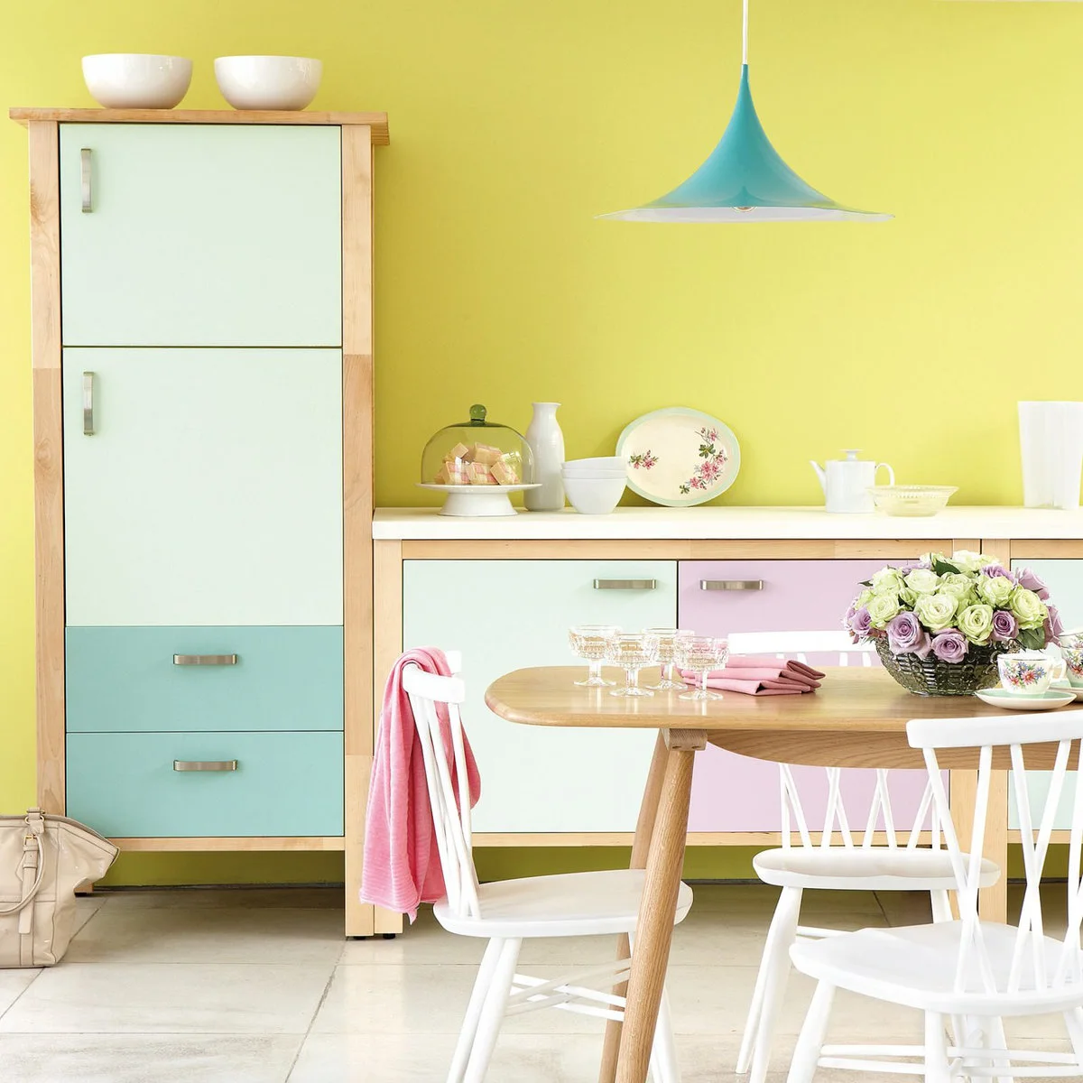 Pastel kitchen cabinets in mint, blue and lilac beneath a yellow wall with a wood-colored dining table