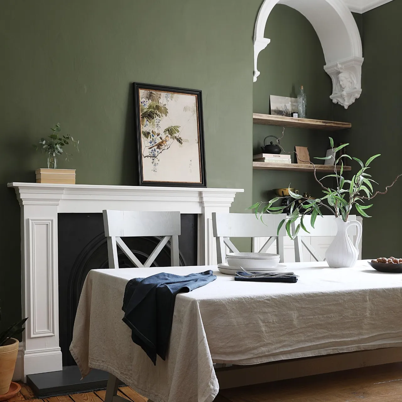 Green dining room with white mantel, botanical picture and pale table and chairs