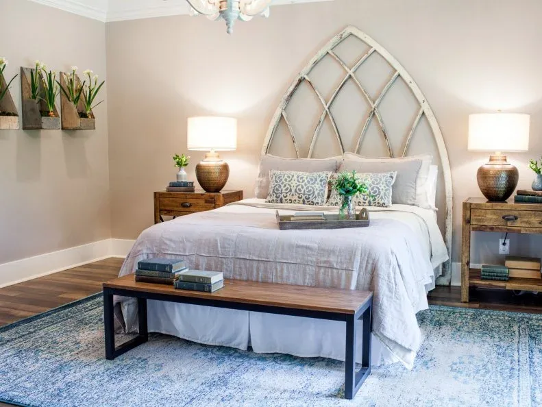 Pale bedroom with wood bedside units, broad lamps, light bedding and an arched frame above the bed