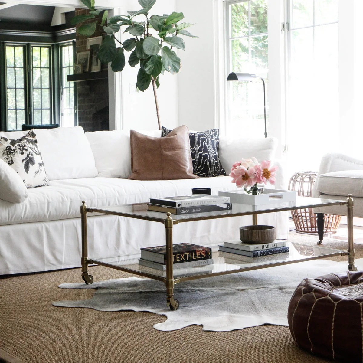 Glass coffee table with a white flower tray above books on a lower shelf