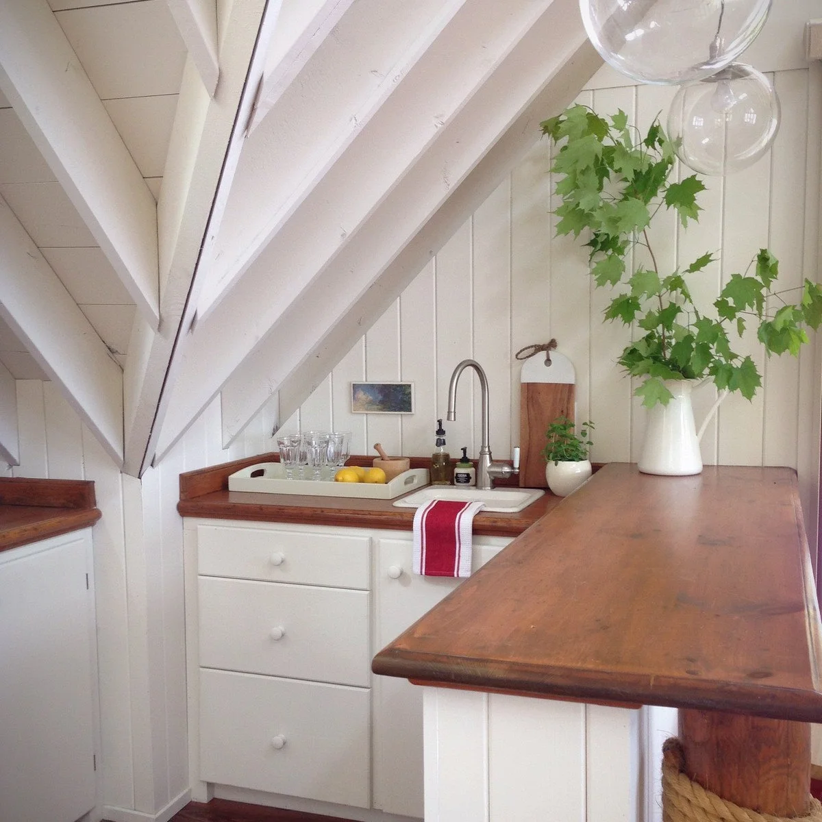 White kitchenette cabinets and a wood counter with a small sink beneath a sloping ceiling